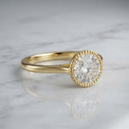3 CT round lab grown diamond engagement ring in a beaded milgrain bezel setting in yellow gold resting on white marble.