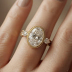On-finger view of a 3 carat oval lab diamond ring featuring a beaded milgrain bezel rim and engraved leaf-motif yellow gold band.