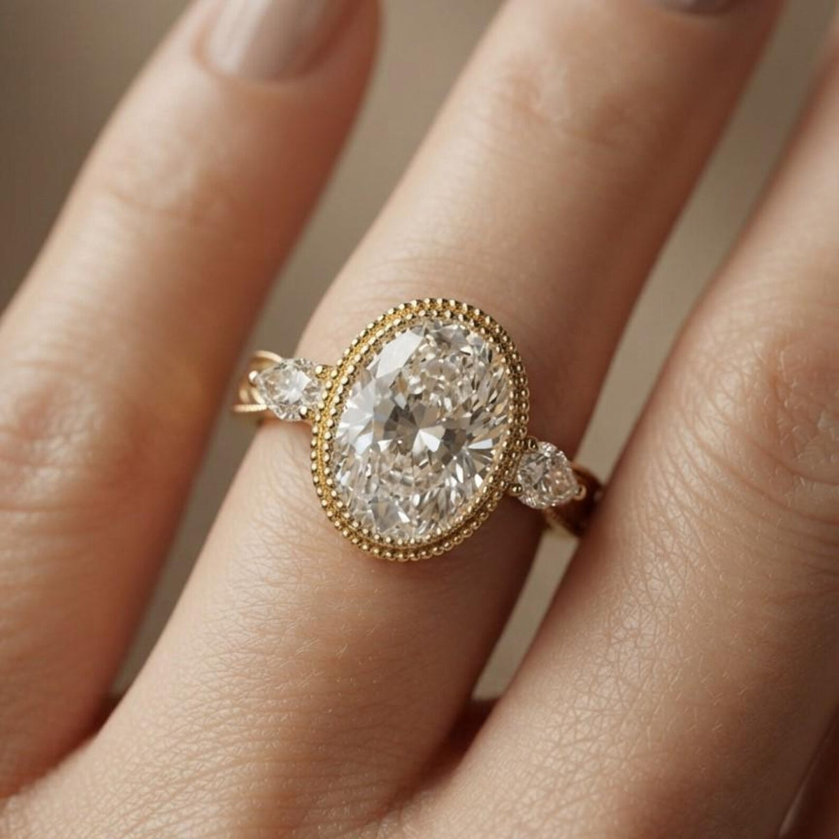 On-finger view of a 3 carat oval lab diamond ring featuring a beaded milgrain bezel rim and engraved leaf-motif yellow gold band.