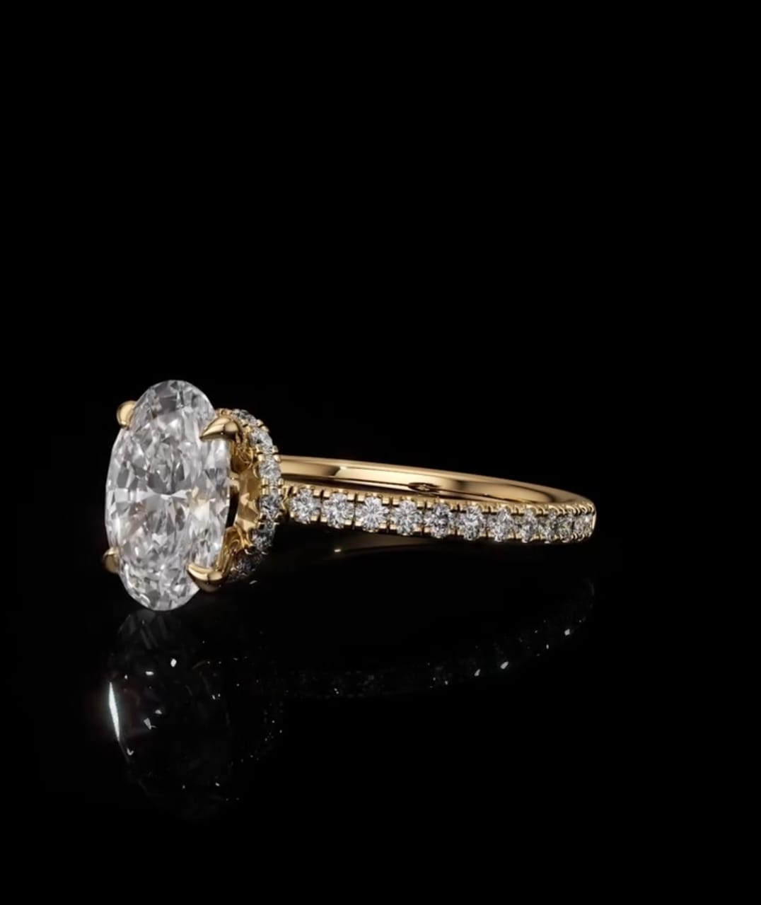 A yellow gold ring featuring a large oval-cut clear gemstone in a prong setting, with a pavé band of smaller round stones, photographed on a reflective black background.