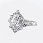 Angled view of a white gold 3 CT pear cut lab grown diamond ring with starburst filigree halo and hand-engraved band.