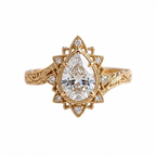 Top-down view of a 3 CT pear cut lab grown diamond engagement ring with starburst halo and engraved band in yellow gold.