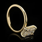 High-angle side view of a 4 CT emerald cut solitaire ring highlighting the clean, modern setting and sparkling hidden halo collar