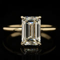 Close-up view of a 4 CT emerald cut lab-grown diamond engagement ring displaying step-cut facets and a subtle diamond hidden halo on a polished yellow gold band.