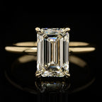 Close-up view of a 4 CT emerald cut lab-grown diamond engagement ring displaying step-cut facets and a subtle diamond hidden halo on a polished yellow gold band.