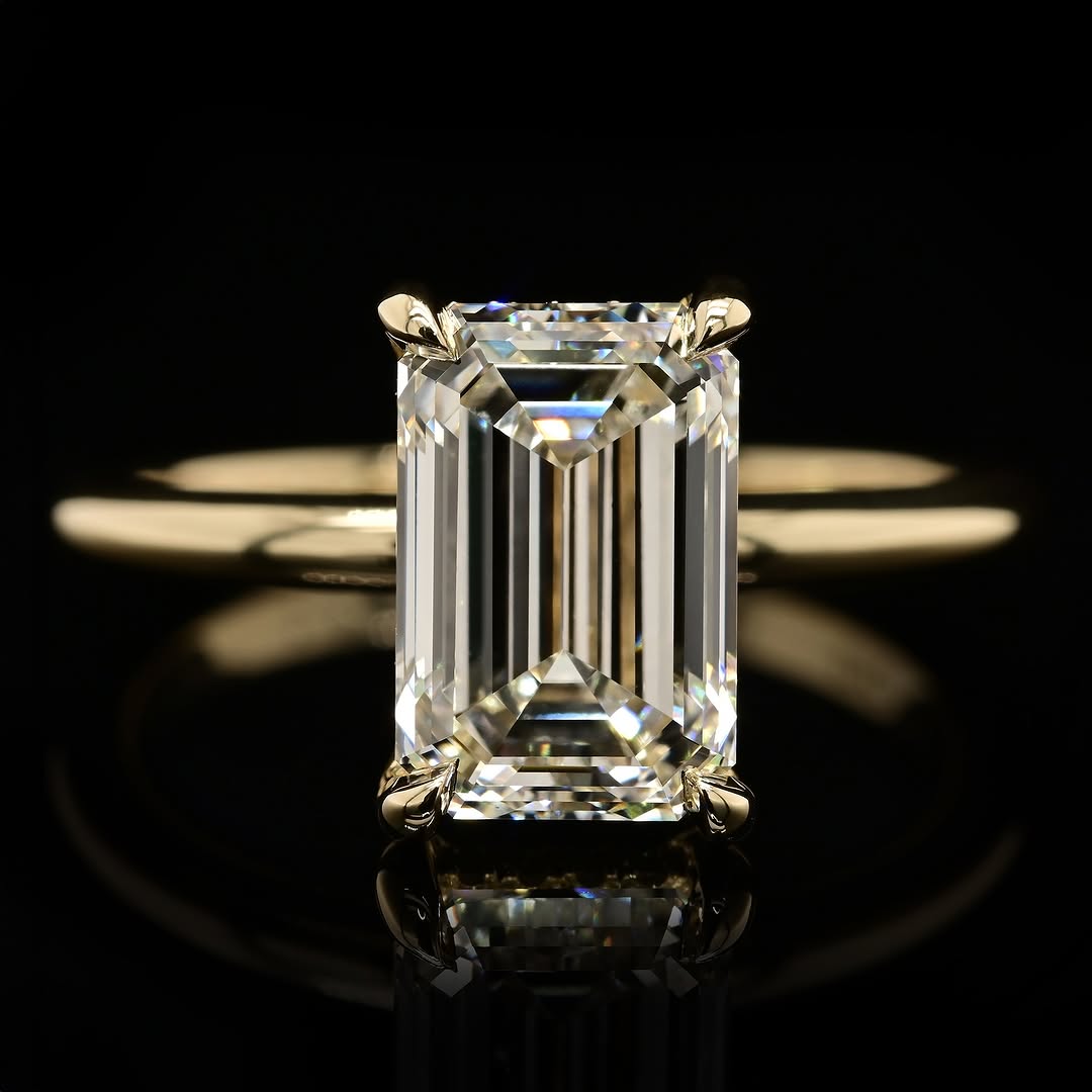 Close-up view of a 4 CT emerald cut lab-grown diamond engagement ring displaying step-cut facets and a subtle diamond hidden halo on a polished yellow gold band.