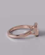 A rose gold ring with a geometric, triangular-prong setting holding a clear gemstone, shown from a side profile on a neutral gray background.