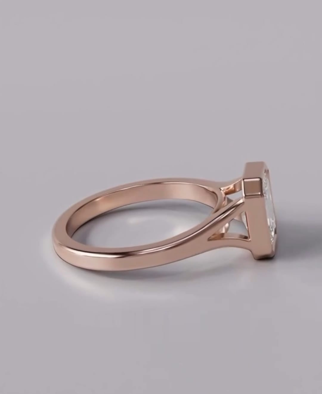 A rose gold ring with a geometric, triangular-prong setting holding a clear gemstone, shown from a side profile on a neutral gray background.
