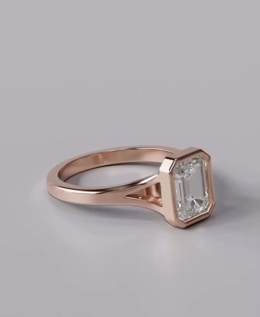 A rose gold ring featuring an emerald-cut clear gemstone, shown on a neutral gray background.