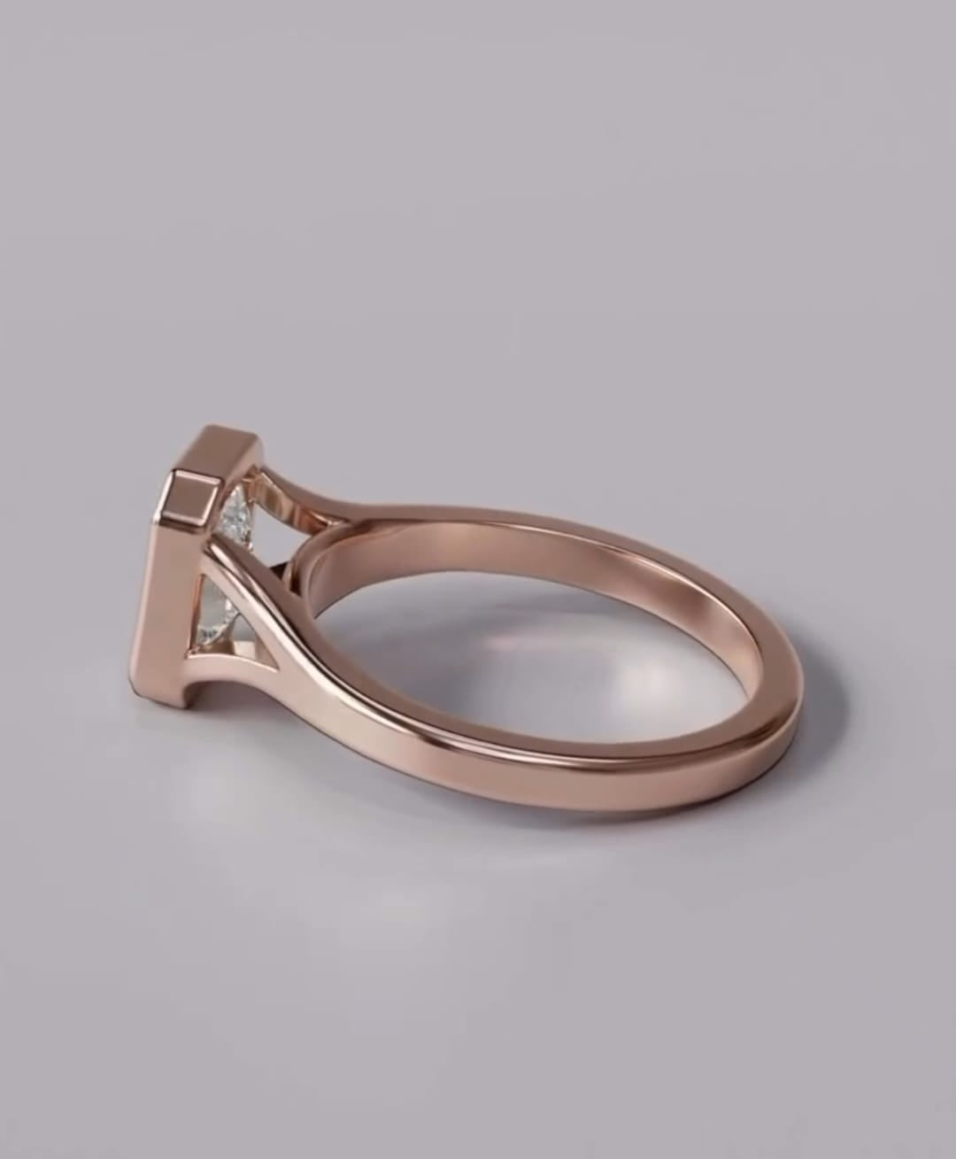 A rose gold ring with a geometric, angular setting and clear triangular gemstones, shown on a neutral gray background.