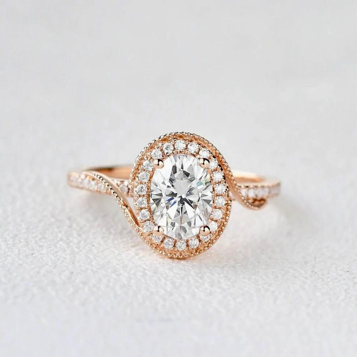 Front view of a 2 CT oval cut lab grown diamond engagement ring in 14K rose gold featuring a bypass swirl halo with milgrain border.