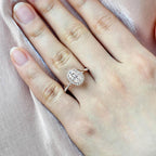 On-hand view of a 2 carat oval lab diamond bypass halo engagement ring in rose gold worn on a finger.
