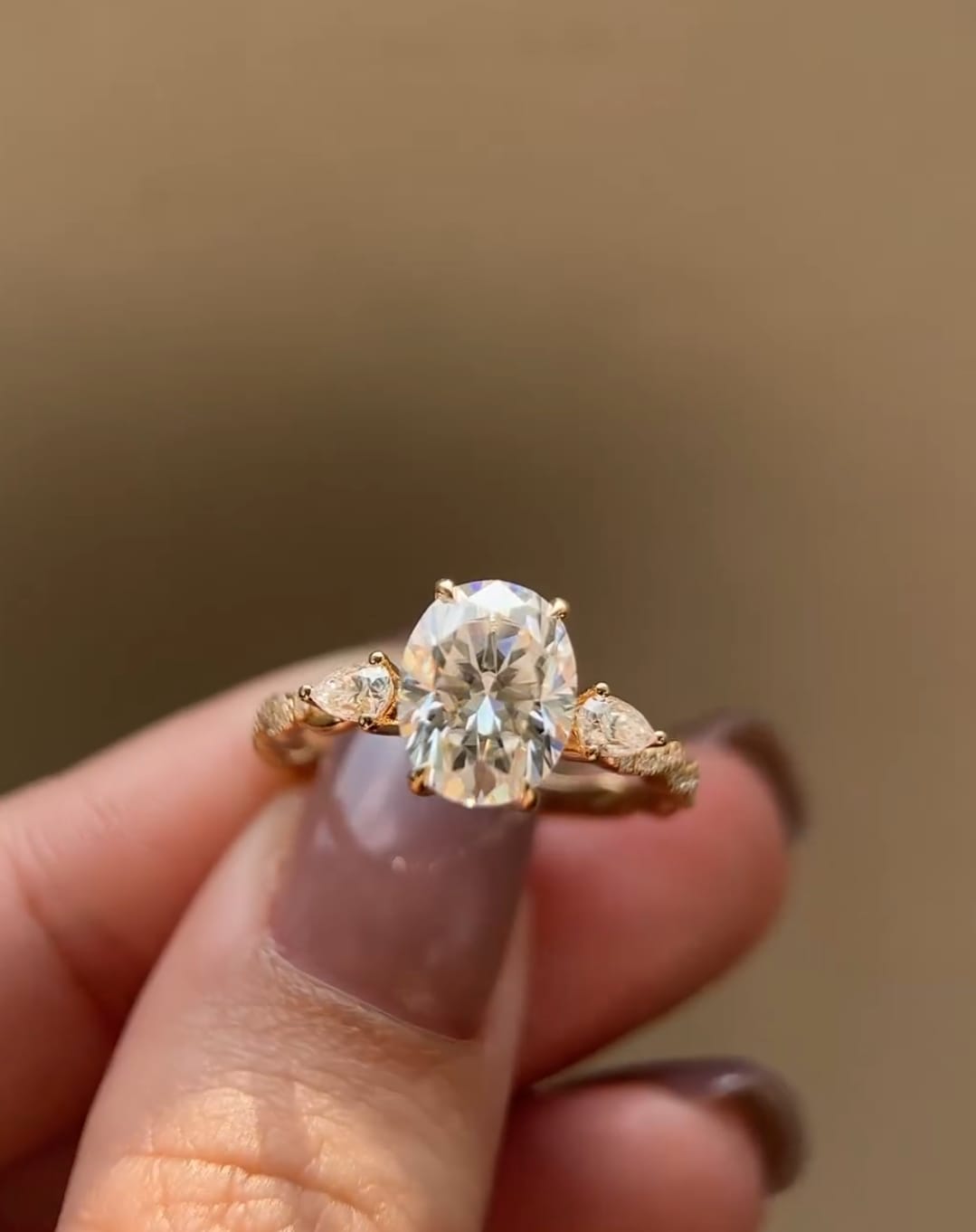 Close-up of a 2 CT oval lab grown diamond engagement ring with pear side accents and twisted pave band held on hand.