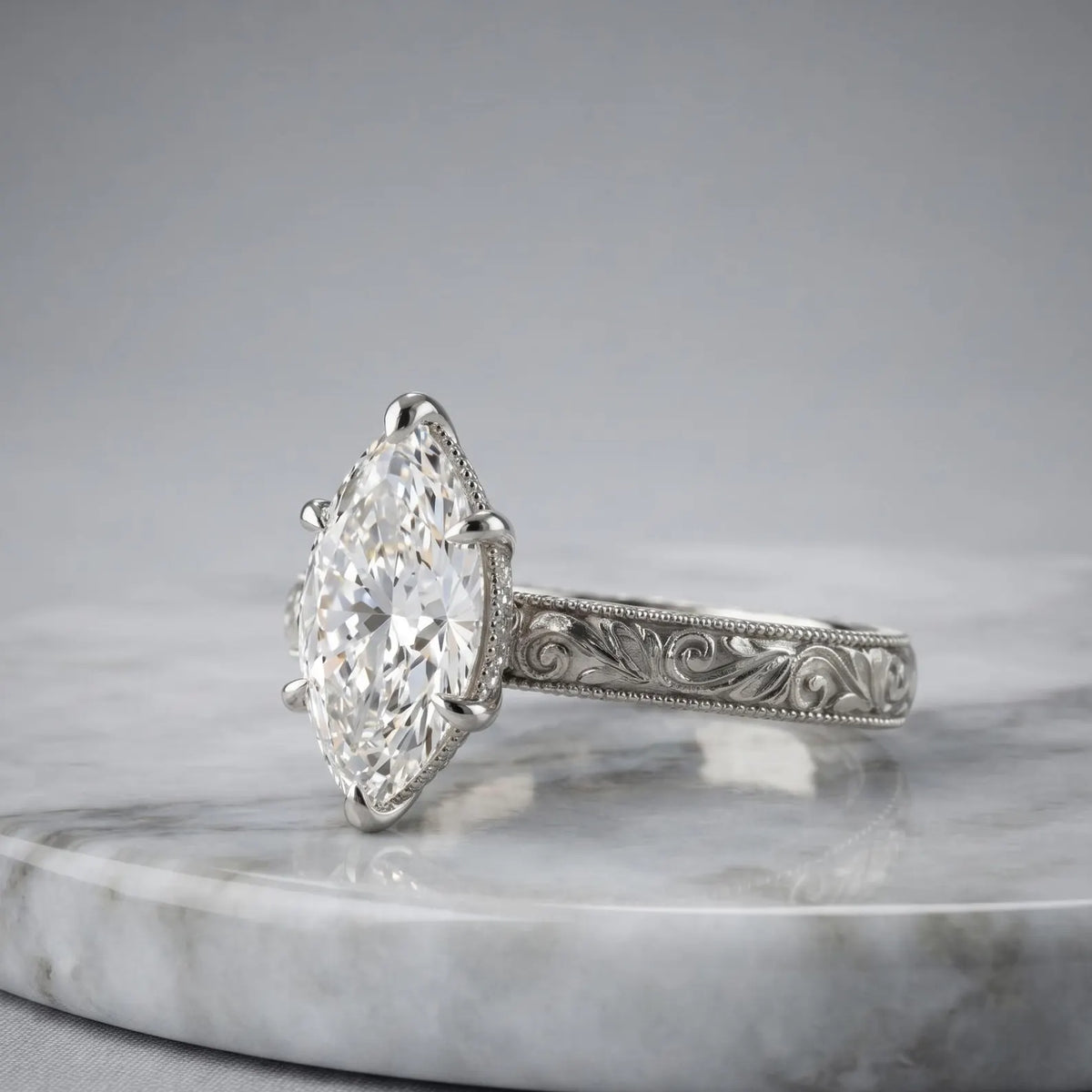 Side view of a 4 CT marquise cut lab grown diamond engagement ring with hand engraving in platinum on a marble surface.