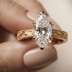 Front view on hand showing a 4 CT marquise lab diamond solitaire ring with floral scroll engraving in yellow gold.