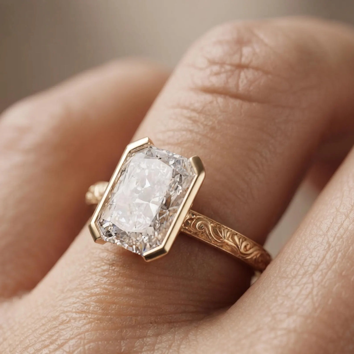 On-finger shot of a 3 CT radiant cut lab grown diamond ring with half bezel setting and hand-engraved yellow gold band.
