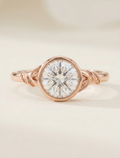 Top-down view of a 3 CT round lab grown diamond ring with full bezel setting and leaf motif shoulders in rose gold.