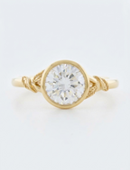 Top view of a 3 CT round cut lab grown diamond bezel engagement ring with carved leaf details in yellow gold.