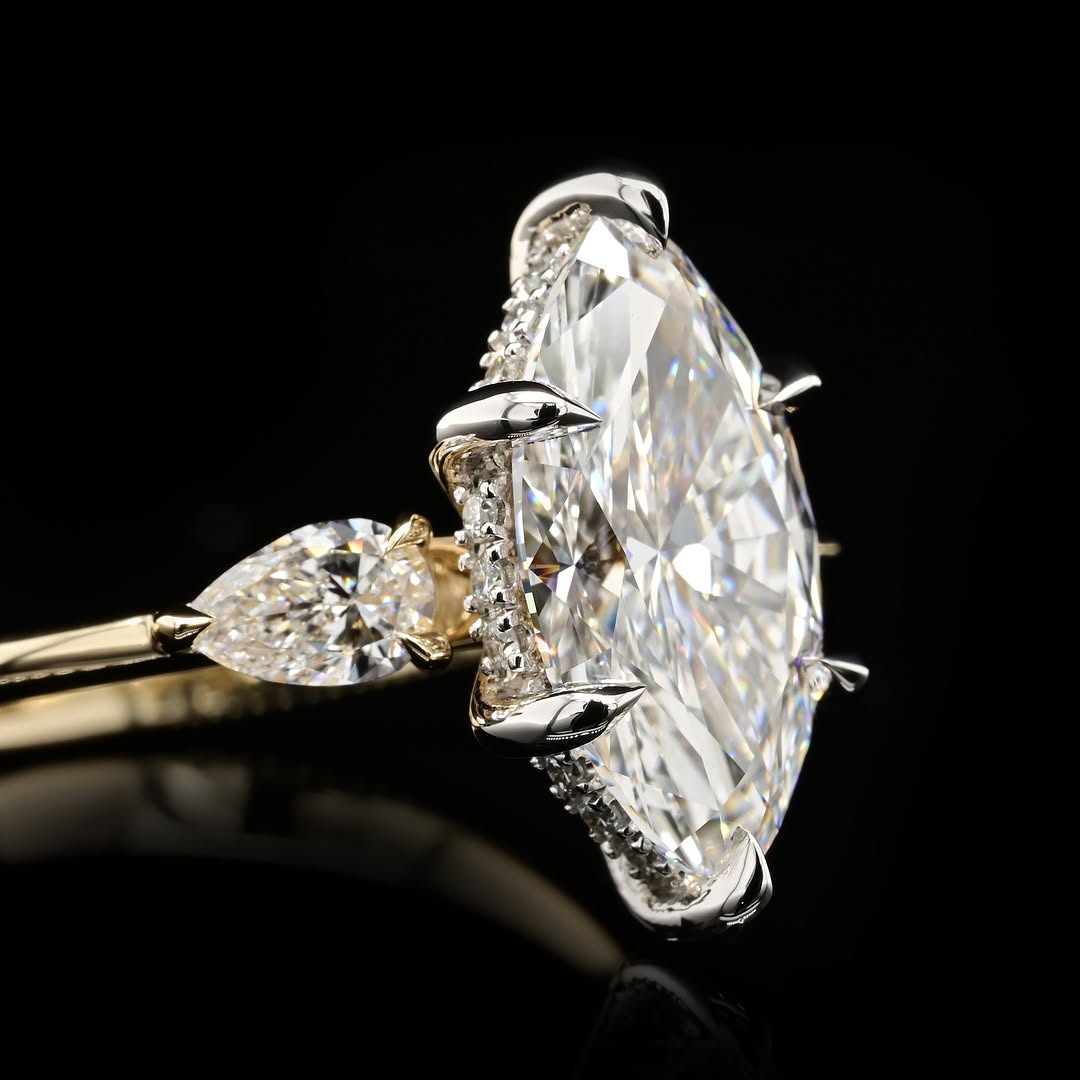 Close-up side perspective showing the six-prong platinum/white gold head, protective V-prongs, and a delicate pave diamond hidden halo surrounding the marquise center stone.