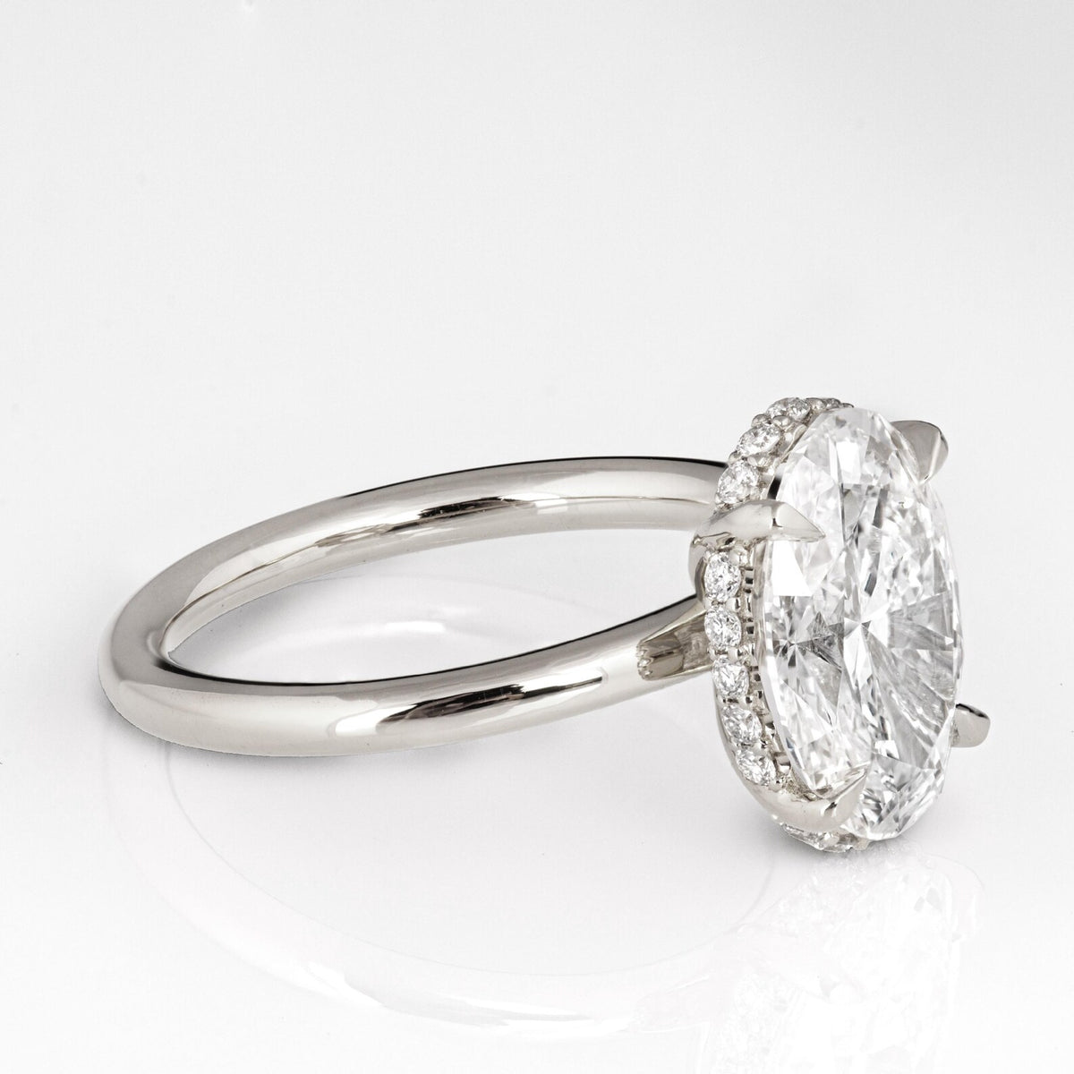 Side angle view of a 3 CT oval lab diamond ring showing micro-pave hidden halo collar and claw prongs.