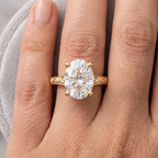 Top-down view on finger displaying a 3 CT oval cut lab grown diamond solitaire ring with round gold prongs.