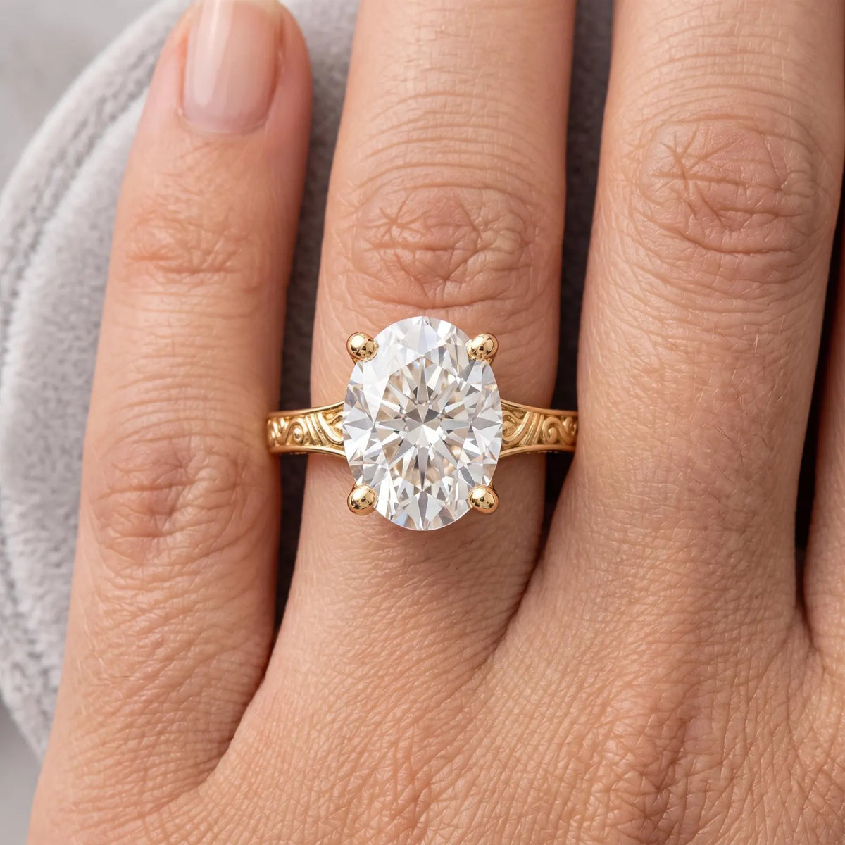Top-down view on finger displaying a 3 CT oval cut lab grown diamond solitaire ring with round gold prongs.