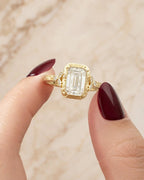 Close-up of a hand holding a 4 CT emerald cut lab grown diamond ring with hand-engraved yellow gold bezel.