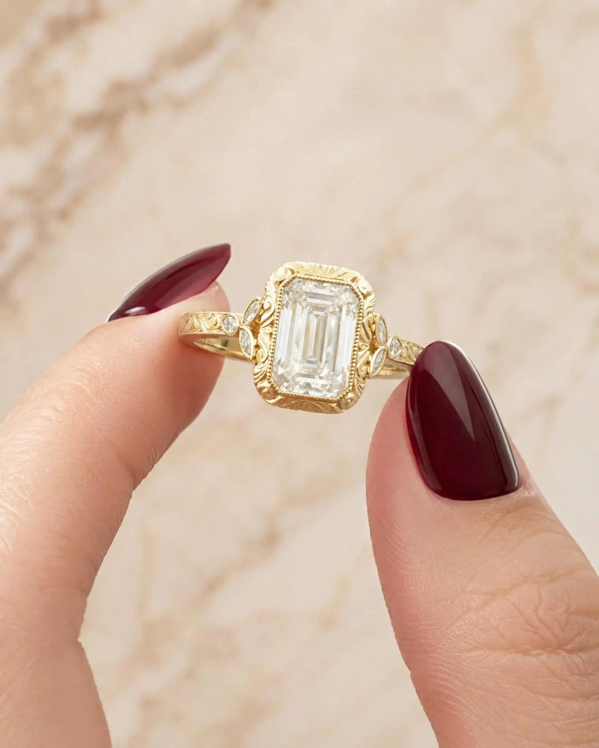 Close-up of a hand holding a 4 CT emerald cut lab grown diamond ring with hand-engraved yellow gold bezel.