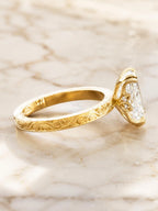 Side profile angle showing hand-engraved scrollwork band and hidden floral gallery accent on a yellow gold cushion diamond ring.