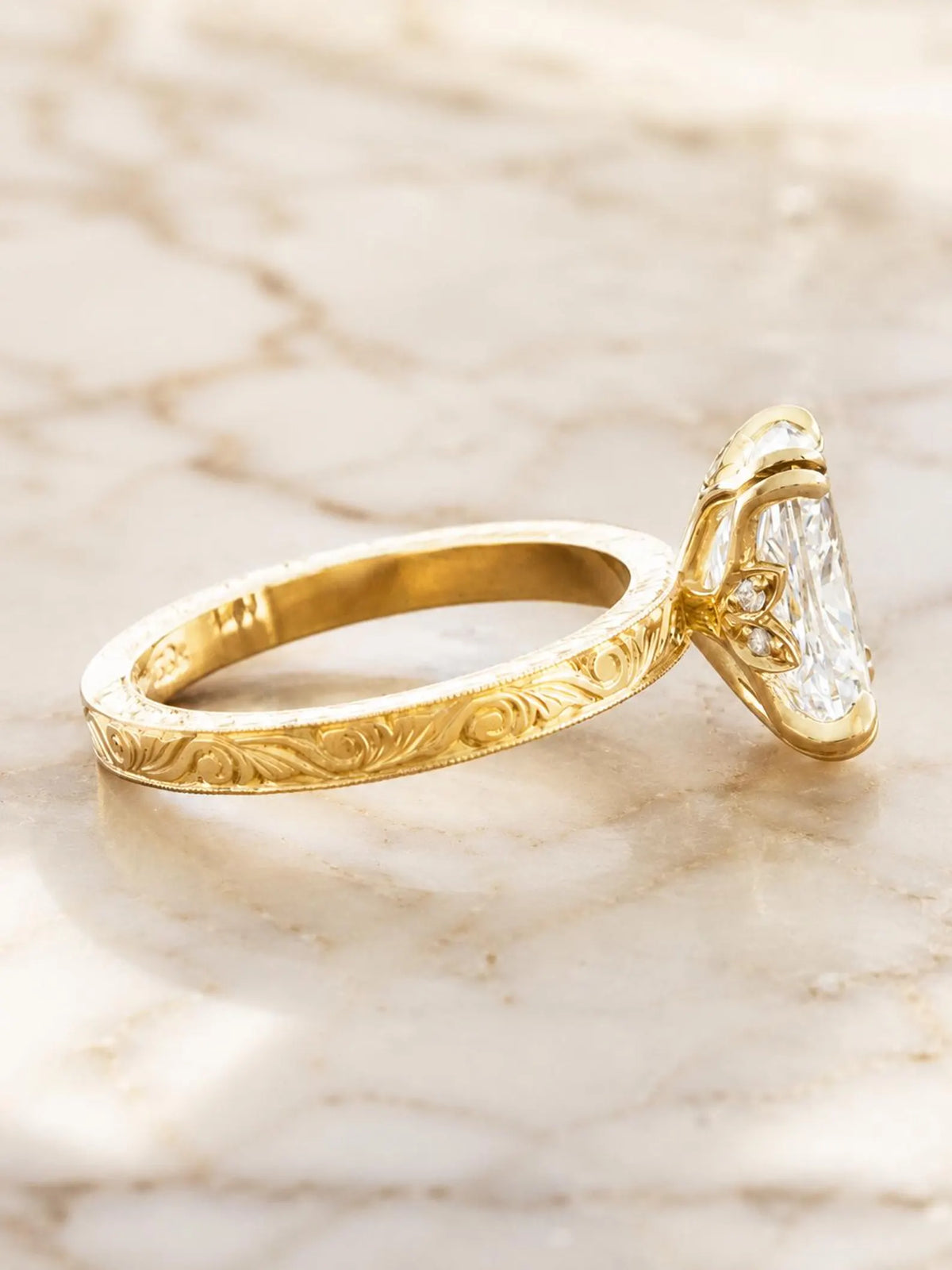 Side profile angle showing hand-engraved scrollwork band and hidden floral gallery accent on a yellow gold cushion diamond ring.