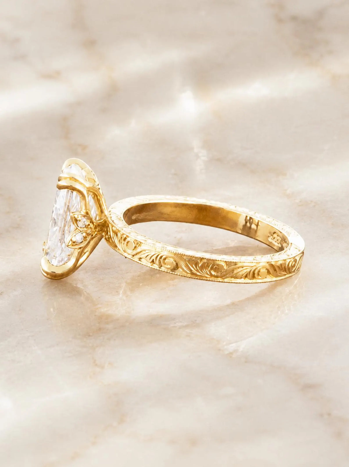 Angled side view showing intricate hand-carved scrollwork and double claw prong detail on 14K yellow gold band.