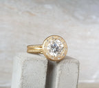 Angled side profile view of 4 CT round lab grown diamond ring set in a brushed gold accent bezel with beaded band.