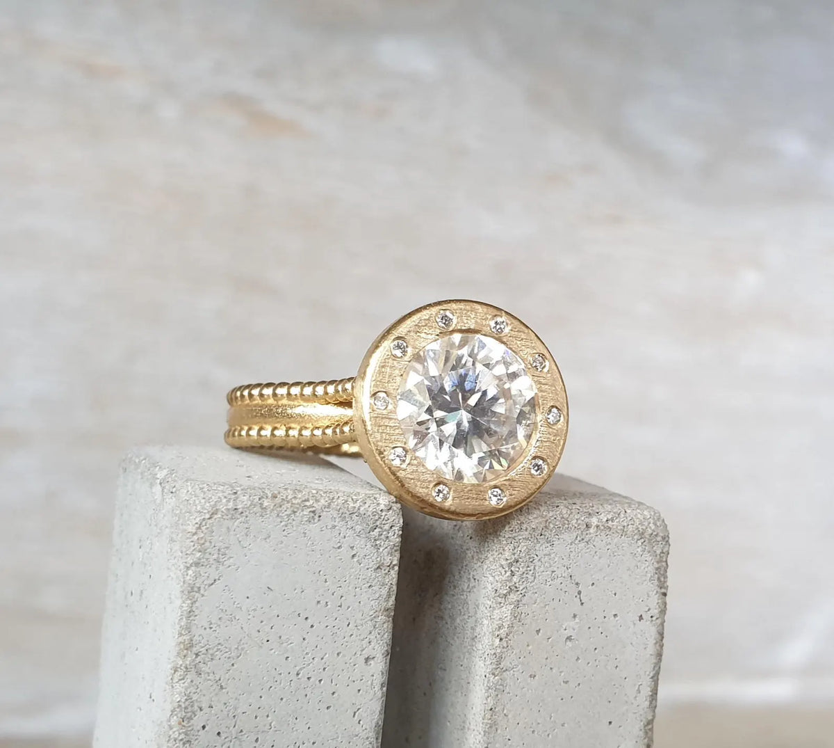 Angled side profile view of 4 CT round lab grown diamond ring set in a brushed gold accent bezel with beaded band.