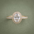 Direct front view of an oval cut lab grown diamond framed by a gold bezel lip and sparkling halo ring.