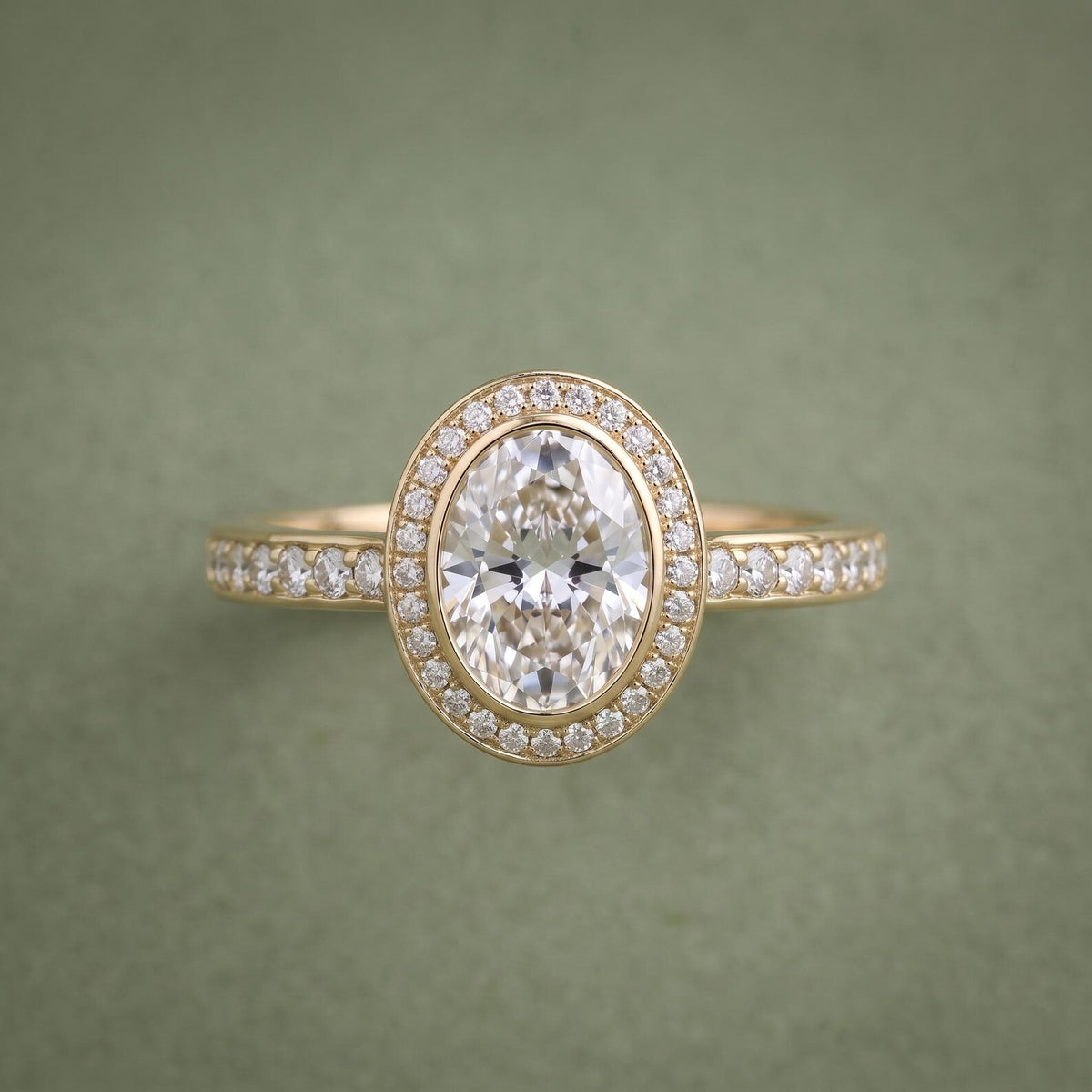 Direct front view of an oval cut lab grown diamond framed by a gold bezel lip and sparkling halo ring.
