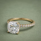 Three-quarter top view of a 3 CT cushion cut lab grown diamond ring with pavé band in 14K yellow gold.