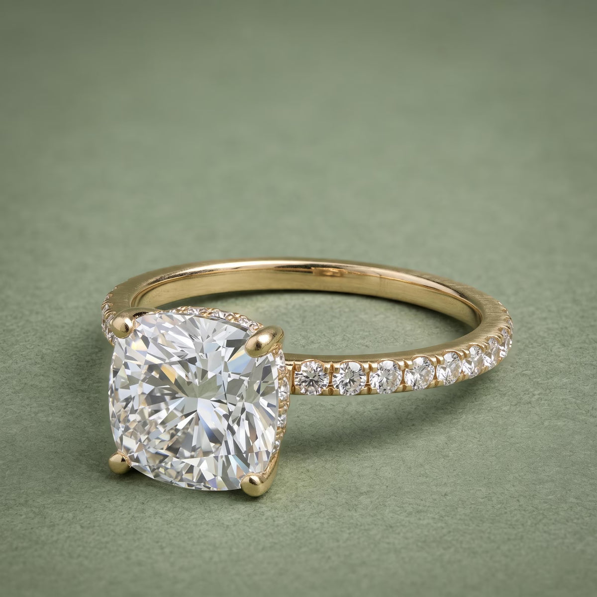 Three-quarter top view of a 3 CT cushion cut lab grown diamond ring with pavé band in 14K yellow gold.