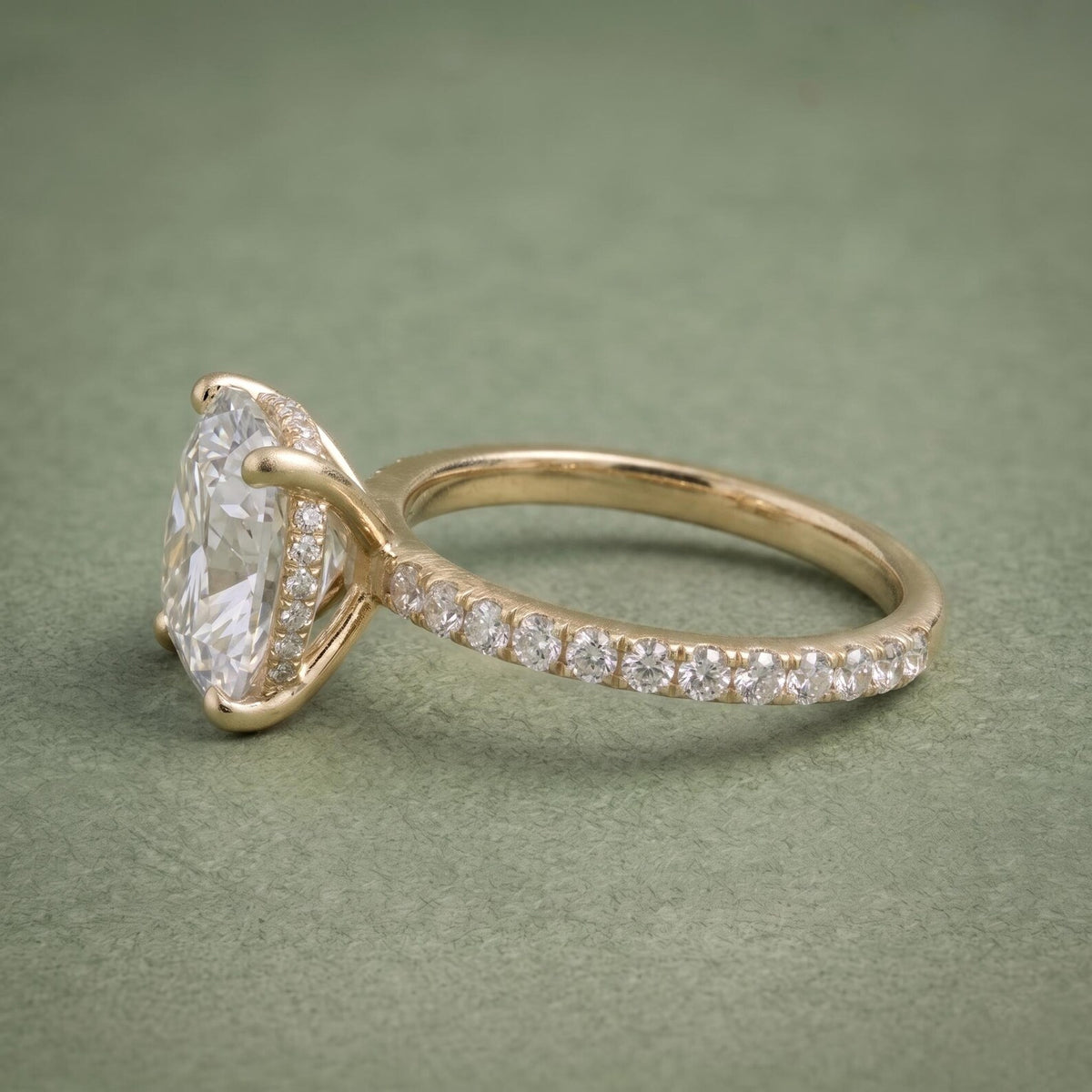 Side profile view of a yellow gold cushion cut diamond ring displaying the hidden halo and pavé shank.