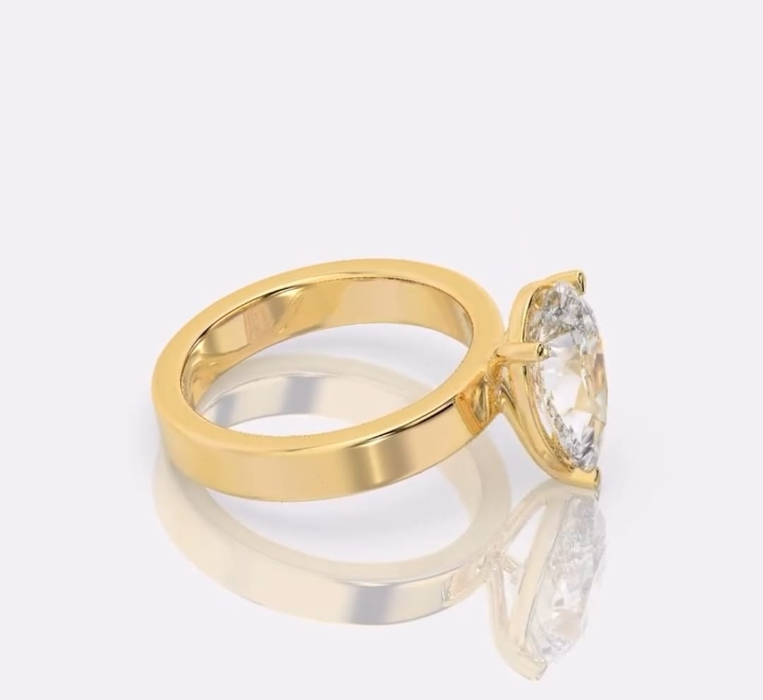 A yellow gold ring with a pear-cut clear gemstone in a prong setting, displayed on a reflective light gray surface against a light gray background.