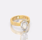 A yellow gold ring featuring a large pear-cut clear gemstone in a prong setting, displayed on a reflective light gray surface.