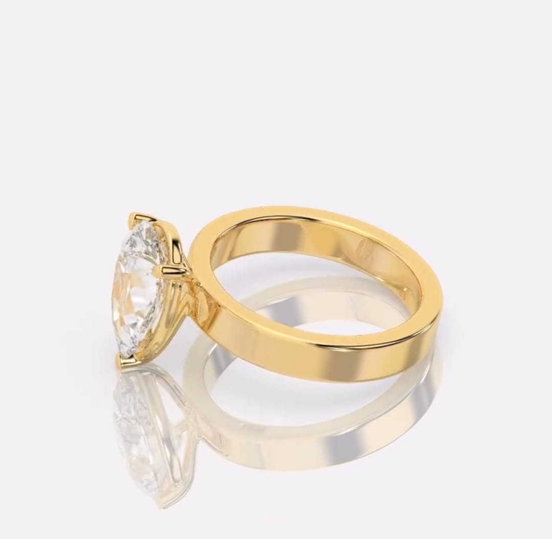 A yellow gold ring with pear -cut clear gemstone, displayed on a reflective light gray surface.