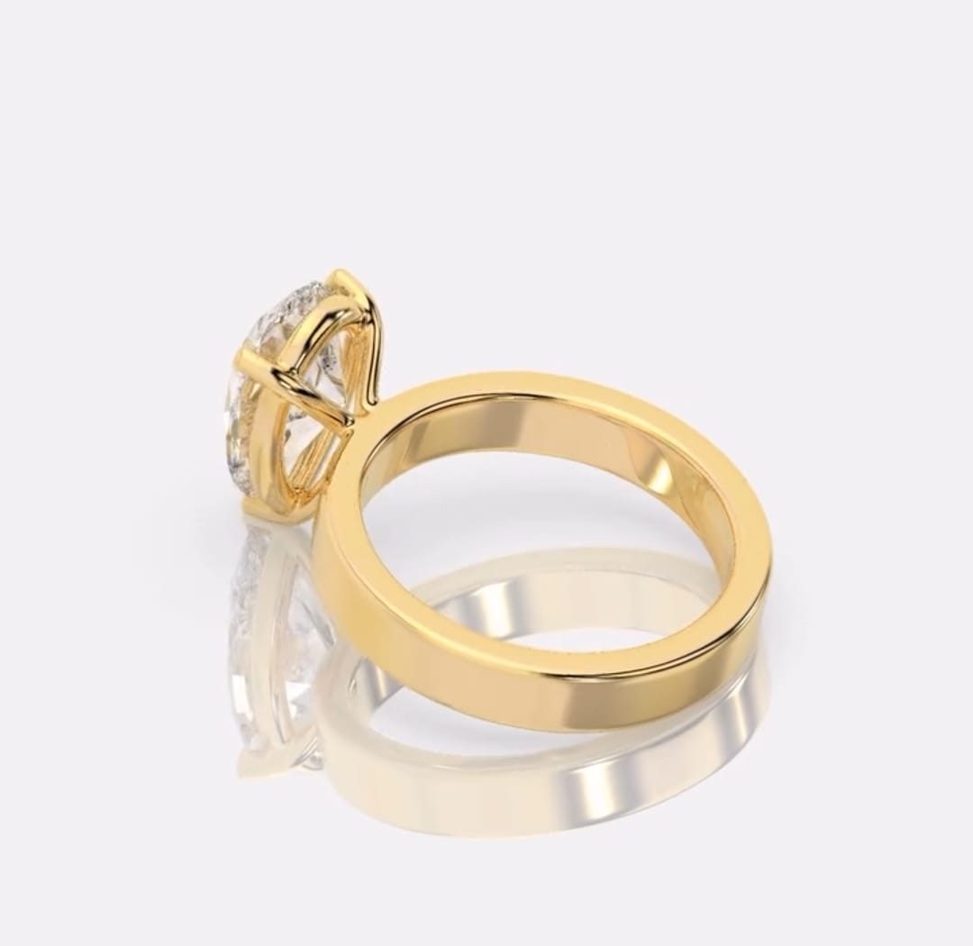 A yellow gold ring with a large clear gemstone in a prong setting, displayed on a reflective light gray surface.