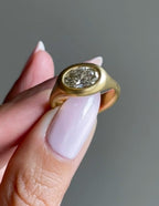 Person holding a modern 2 carat East-West oval diamond signet ring in brushed gold.