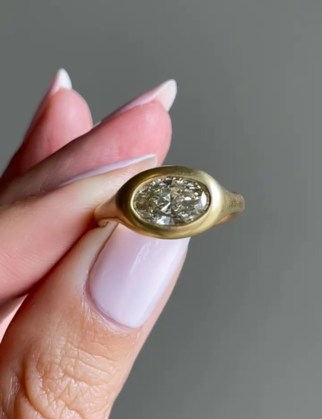 Hand holding a 2 carat East-West oval lab grown diamond ring in a matte gold bezel setting.