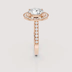 A rose gold ring with a large oval-cut center stone and a halo of small clear stones, featuring a shank paved with round stones, shown on a light gray background.