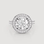 A round halo engagement ring featuring a large round-cut center stone surrounded by a double halo of smaller stones, set in a silver-toned metal band on a light gray background.