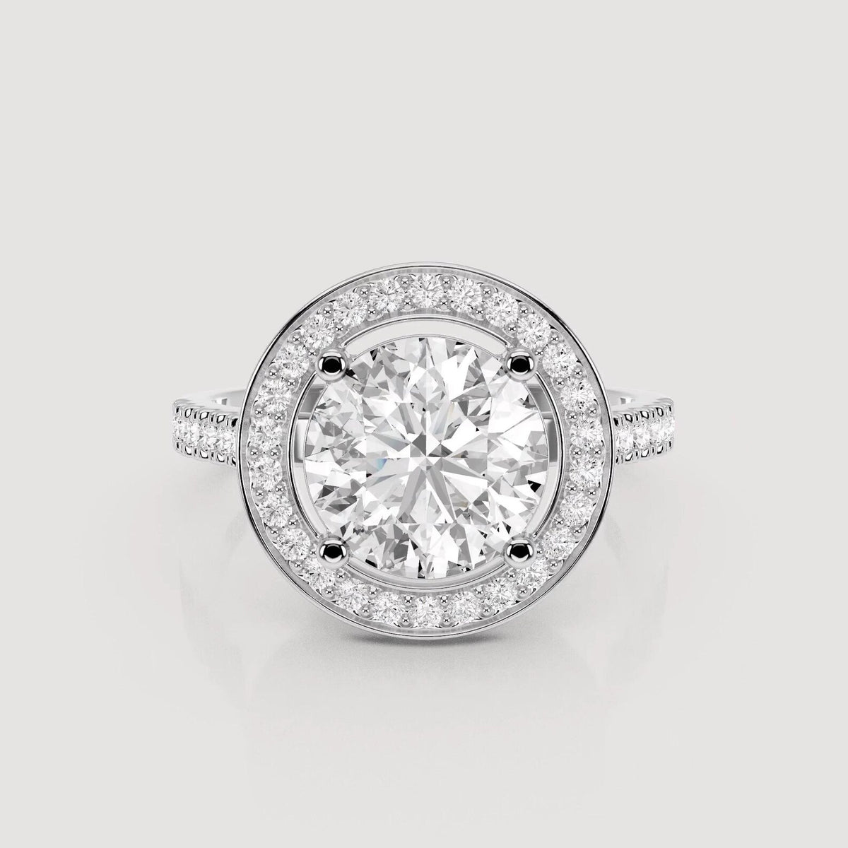 A round halo engagement ring featuring a large round-cut center stone surrounded by a double halo of smaller stones, set in a silver-toned metal band on a light gray background.