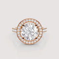 A rose gold halo ring featuring a large round-cut center stone surrounded by a double halo of smaller round stones, with a split shank band also accented with small stones, shown on a light gray background.