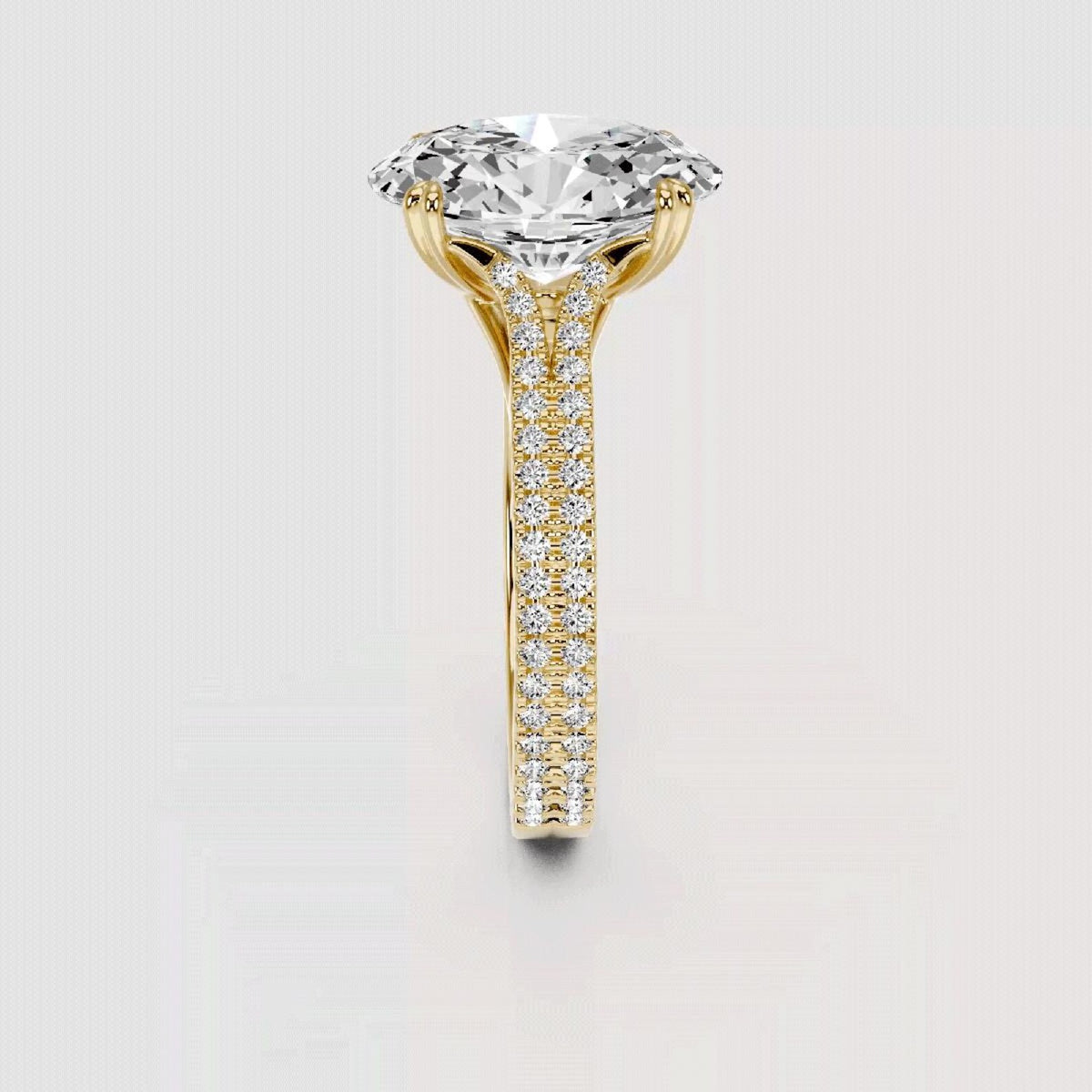 A yellow gold solitaire engagement ring featuring a large round brilliant-cut diamond center stone and a pavé diamond shank, shown on a light gray background.