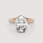 An oval-cut diamond engagement ring in a rose gold setting with a pavé band, shown on a light gray reflective background.